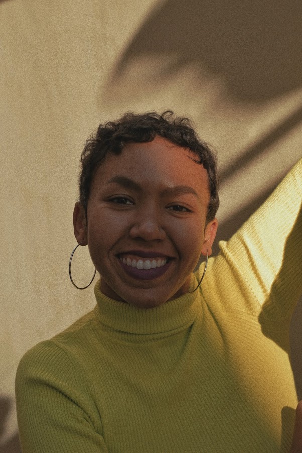 Helena smiling in warm sunlight wearing a yellow turtleneck